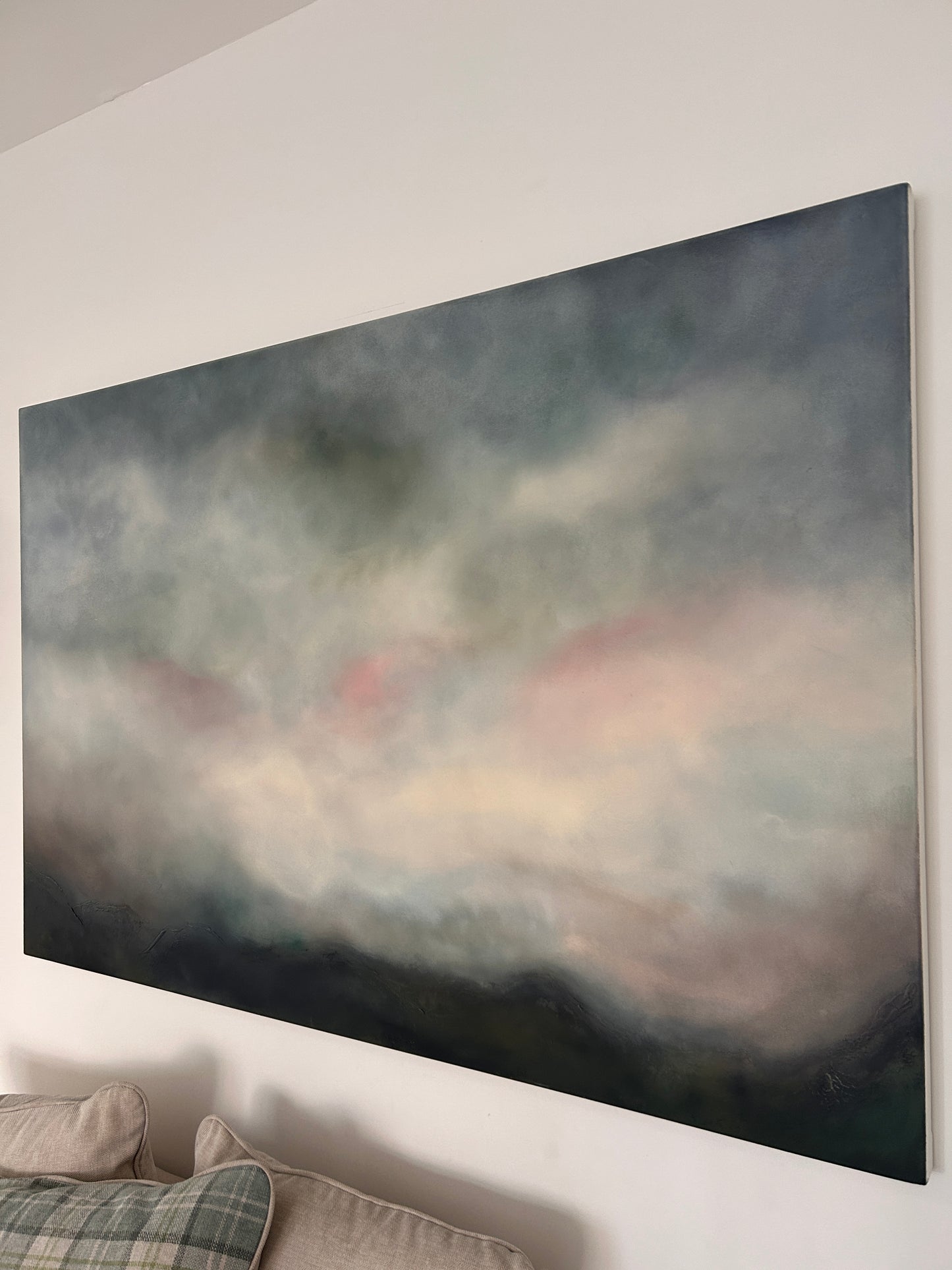 Abstract painting on a white wall with a pillow and blanket in the corner.